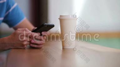 在咖啡馆里，男人手拿着手机和一杯咖啡的特写镜头。 使用移动智能手机的人。 一个男孩摸着屏幕
